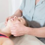 Male manual visceral therapist masseur treats a young female patient. Jaw muscles warm up.